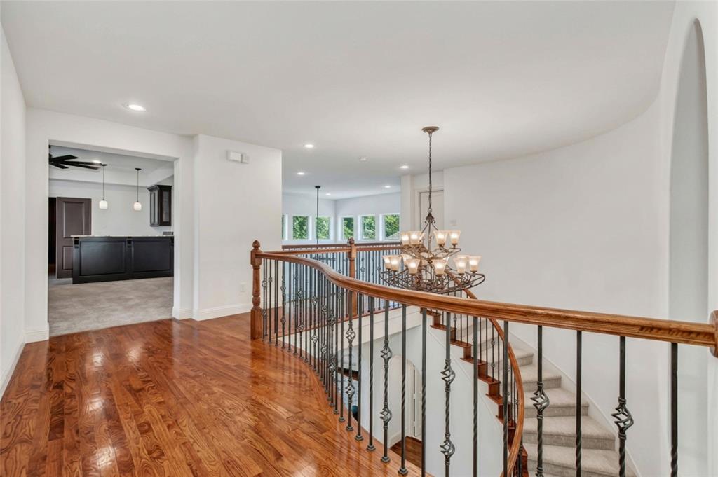 Hardwood flooring, curved staircase with wrought iron balusters, archway, recessed lighting, and chandelier