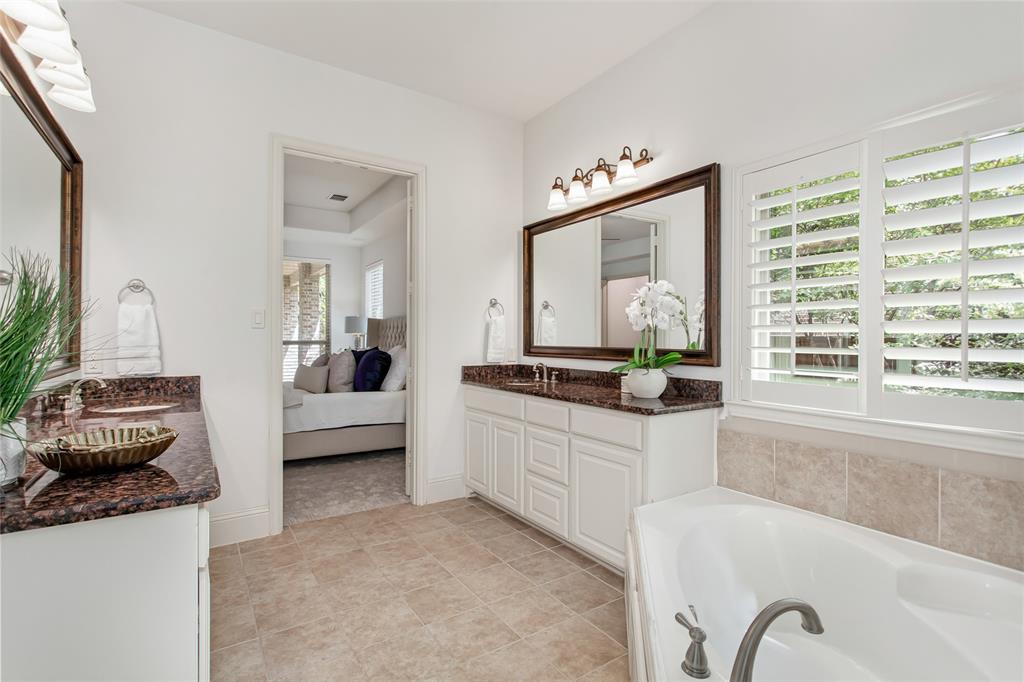 Dual vanity with dark stone countertops, white cabinetry, a large framed mirror, and an adjacent soaking tub