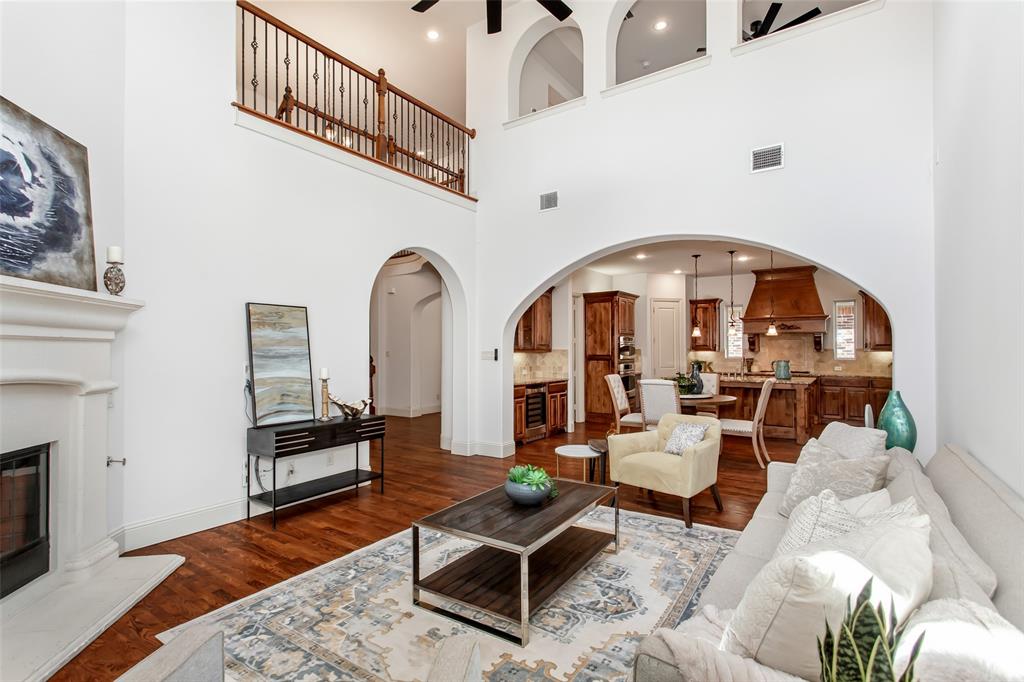 Two-story living area featuring a fireplace with a white mantel, an arched entry to the kitchen, and a second-story landing with an open railing