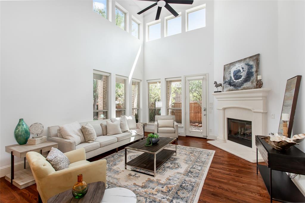 Expansive living area featuring a vaulted ceiling with a ceiling fan, a fireplace with a substantial mantel, multiple windows, and wood-finish flooring