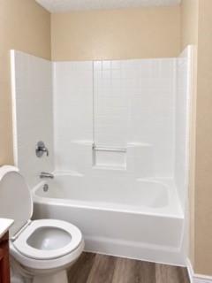 Bathtub with white surround and integrated grab bar, chrome fixtures, and wood-finish flooring