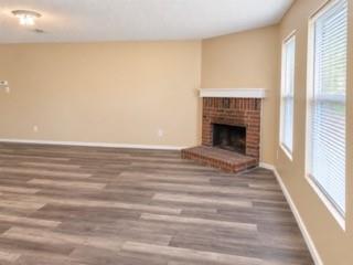 Wood-finish flooring, brick fireplace with a white mantel, and multiple windows with blinds
