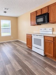Wood-finish flooring, wood cabinetry, white electric range, black microwave, and a single window