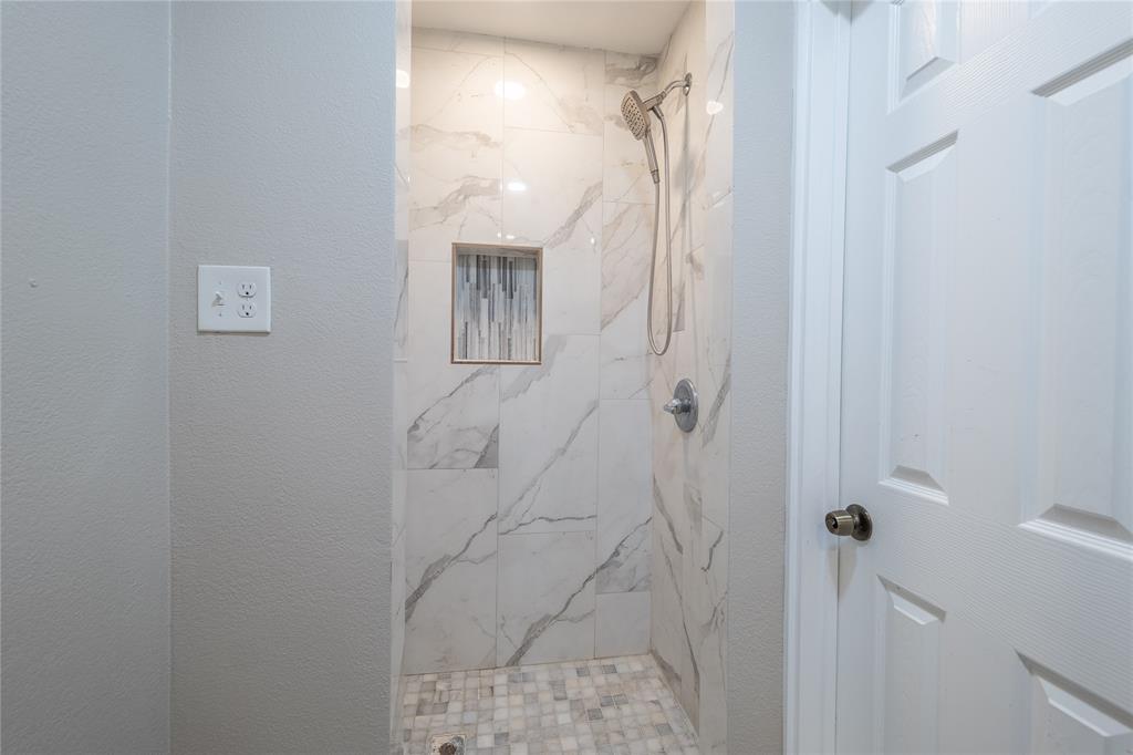 Walk-in shower with large-format tile walls, mosaic tile flooring, a built-in shower niche, and a brushed nickel shower head