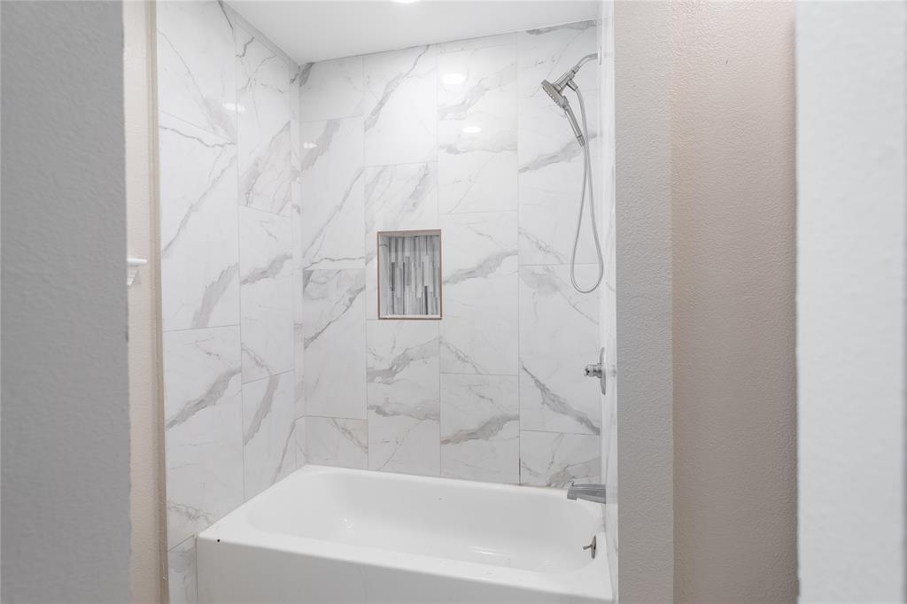 Bathtub with a tiled surround featuring a built-in niche, complete with a showerhead and faucet