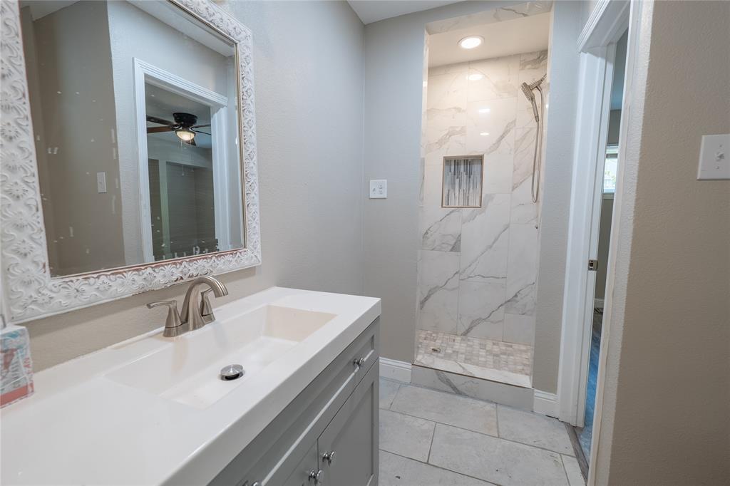 Vanity with integrated sink, brushed nickel faucet, decorative framed mirror, walk-in shower with marble-look tile, and recessed shower niche