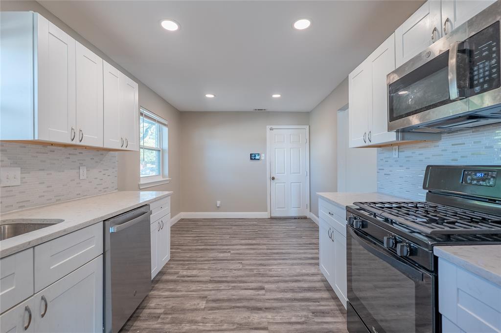 Kitchen featuring white cabinetry, stainless steel appliances, light-toned countertops, tile backsplash, and wood-finish flooring