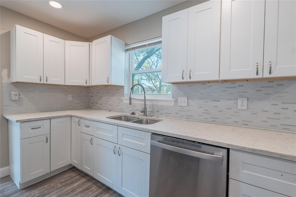 White shaker-style cabinetry, light-toned countertops, stainless steel dishwasher, mosaic tile backsplash, and wood-finish flooring