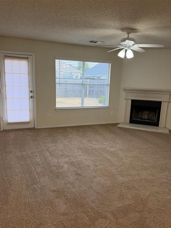 Neutral-toned carpeted flooring, corner-set fireplace with a light-colored mantel, window with horizontal blinds, and a ceiling fan with integrated lighting