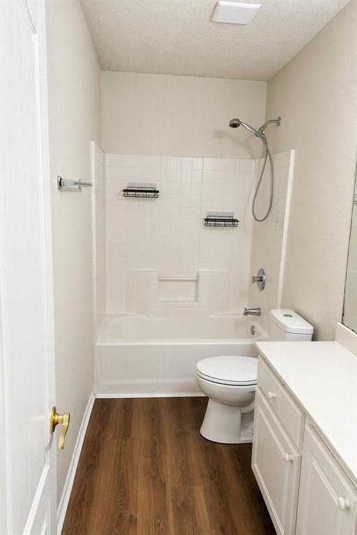Bathroom featuring a white tub/shower combination, white vanity with integrated sink, wood-finish flooring, and chrome fixtures