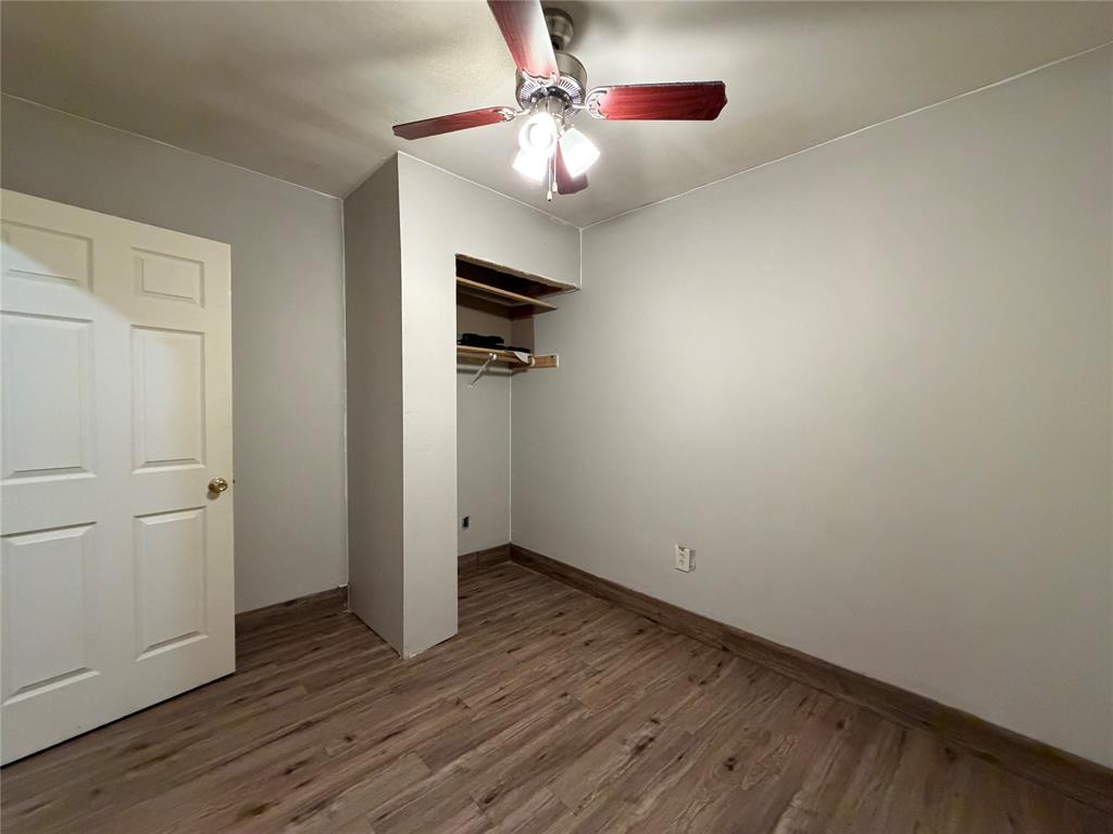 Room featuring wood-finish flooring, light gray walls, built-in open shelving, and a ceiling fan with integrated lighting