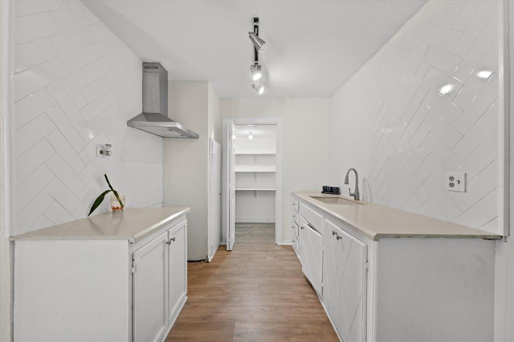 Galley kitchen featuring wood-finish flooring, white cabinetry, light-toned countertops, and a stainless steel range hood