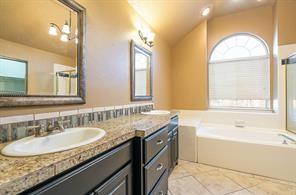 Bathroom with a bath, healthy amount of natural light, tile patterned flooring, vaulted ceiling, and vanity