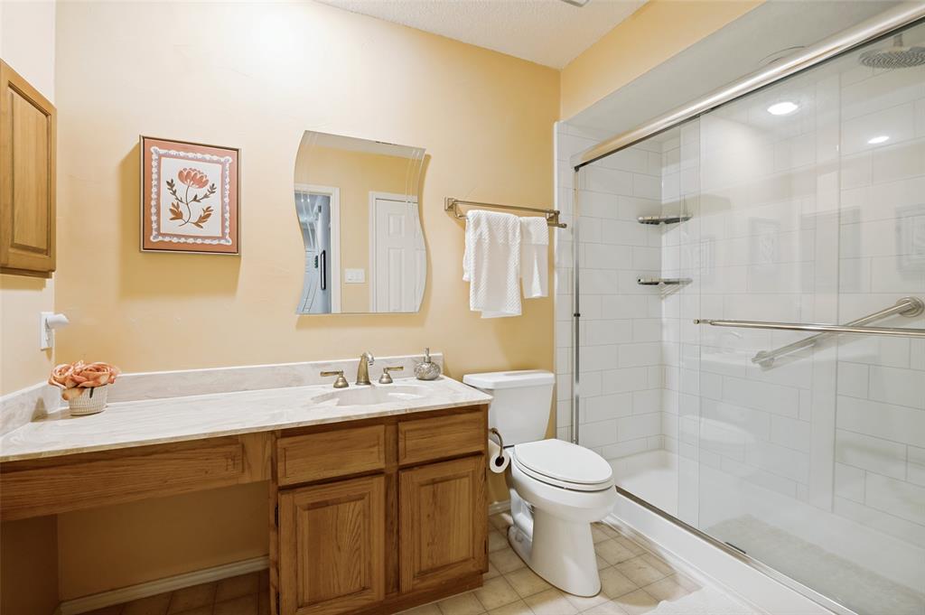 Vanity with integrated sink and wood cabinetry, expansive walk-in shower with clear glass enclosure, tiled shower walls, and a separate toilet area