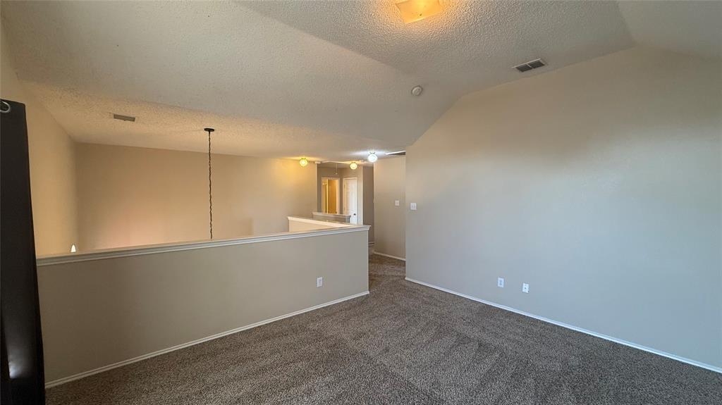 Carpeted flooring, vaulted ceiling, neutral wall tones, interior railing, and overhead lighting