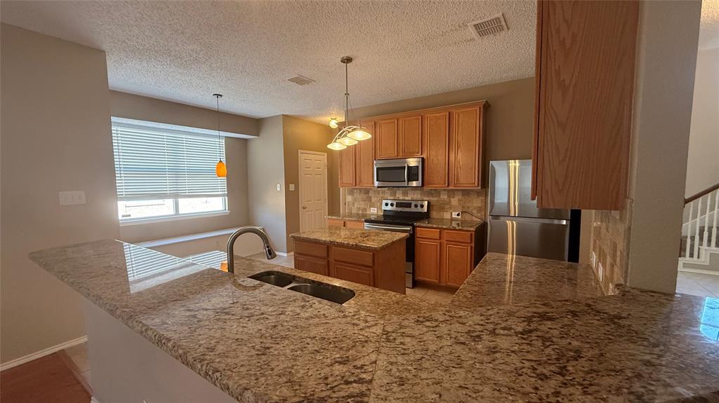 Kitchen featuring granite countertops, wood cabinetry, stainless steel appliances, and a breakfast bar with a double basin sink