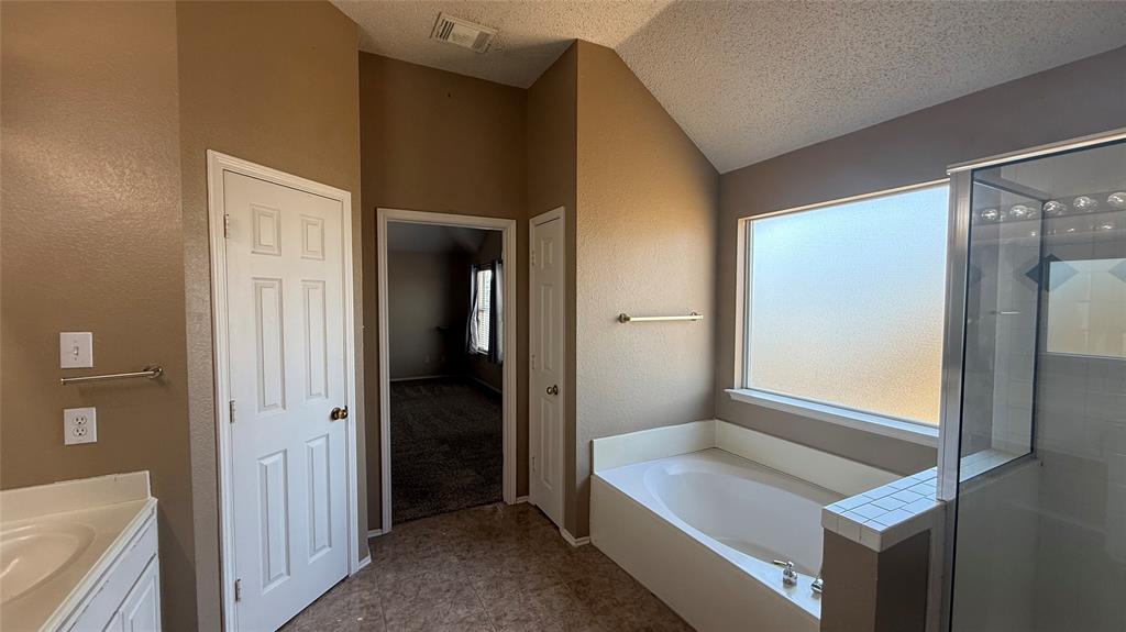 Vaulted ceiling, built-in bathtub, glass-enclosed shower, frosted window, and dual vanity countertop