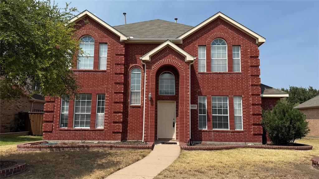 Red brick facade with arched windows, prominent entry archway, and a concrete pathway