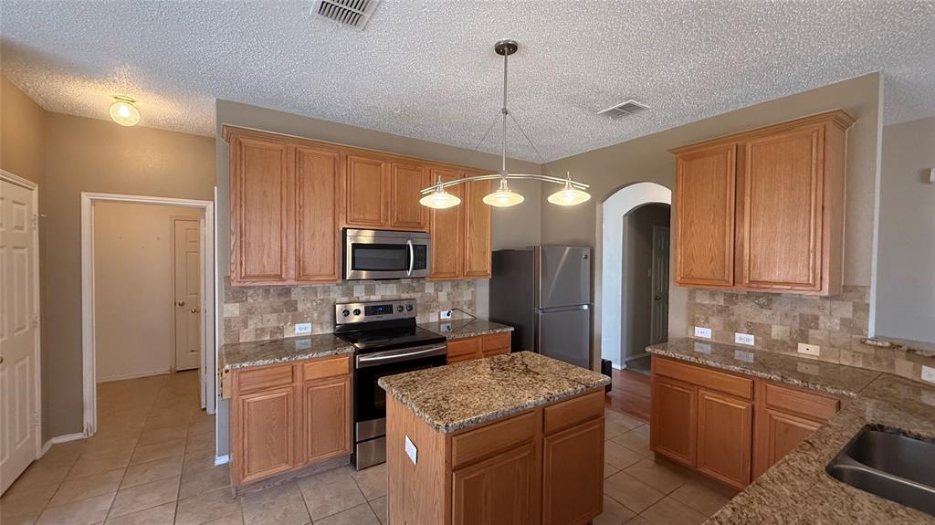 Kitchen featuring an island, light wood-finish cabinetry, stone countertops, stainless steel appliances, and a tile backsplash