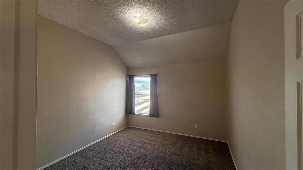 Vaulted ceiling with an attached light fixture, a window with blinds and curtains, and carpet flooring