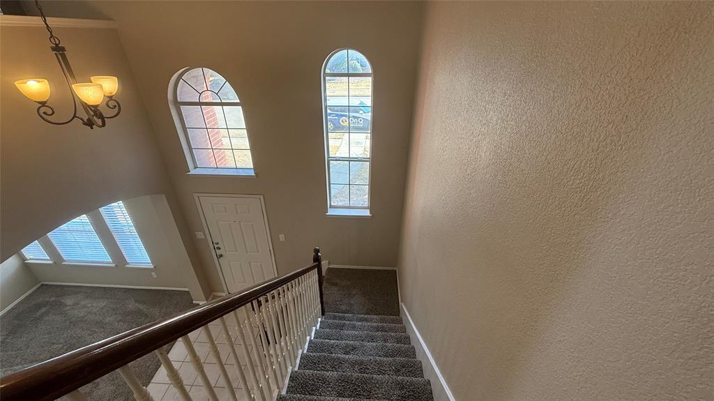 Two-story entry featuring arched windows, a chandelier, and a carpeted staircase with a wood handrail