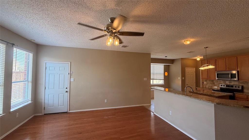 Wood-finish flooring, ceiling fan with integrated lighting, kitchen featuring wood cabinetry, stainless steel appliances, and a stone-finish countertop