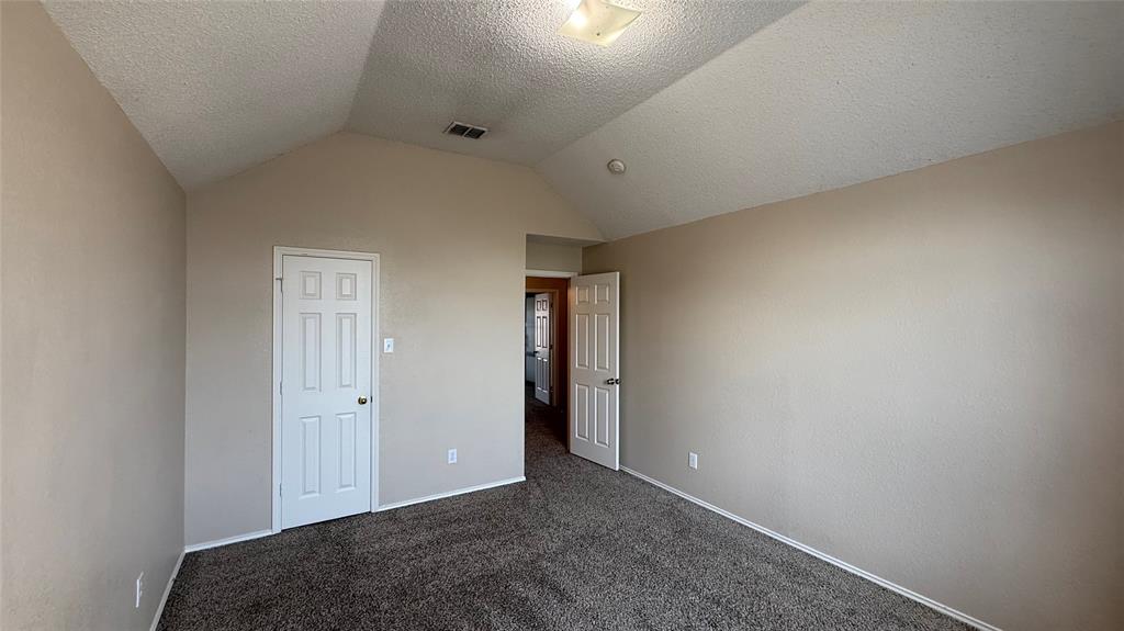 Vaulted ceiling, neutral tone walls, dark carpet flooring, white paneled doors, and a flush mount ceiling light fixture