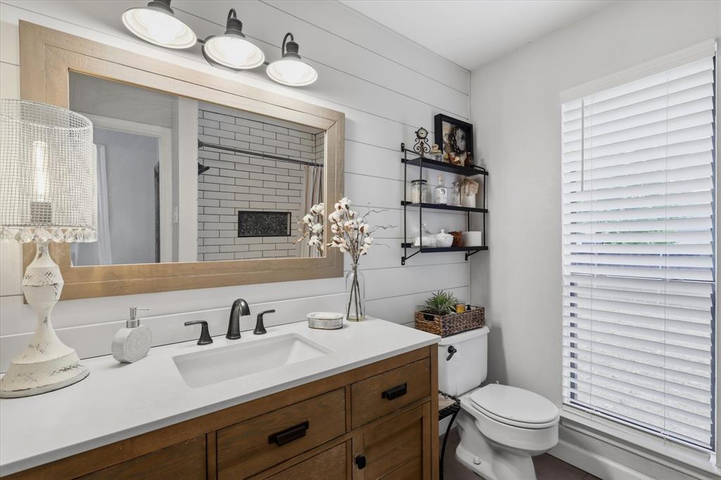 Updated bath pairs a warm wood vanity with a crisp countertop, shiplap accent wall and a beautifully tiled shower.