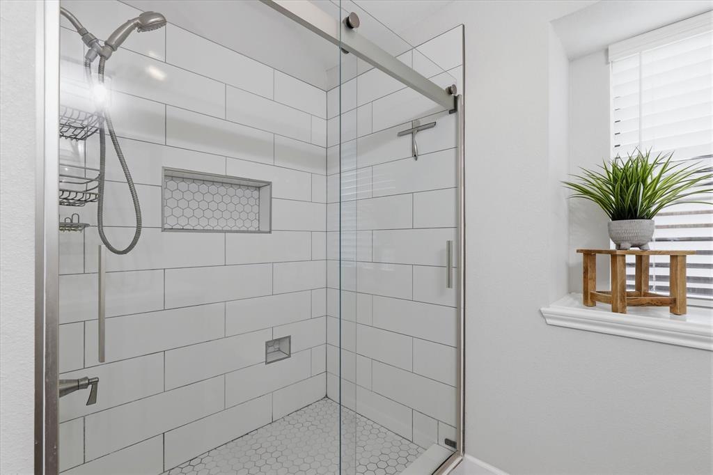 Renovated walk-in shower features frameless glass, oversized tile surround and a decorative tile niche.