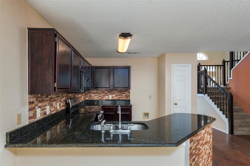 Kitchen featuring dark wood-finish cabinetry, a stone-tile backsplash, and a dark stone-finish countertop with an integrated sink