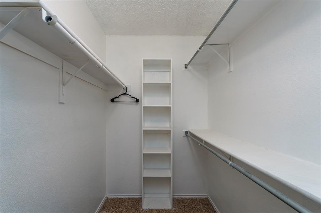 Walk-in closet featuring built-in shelving, white walls, and a textured carpeted floor
