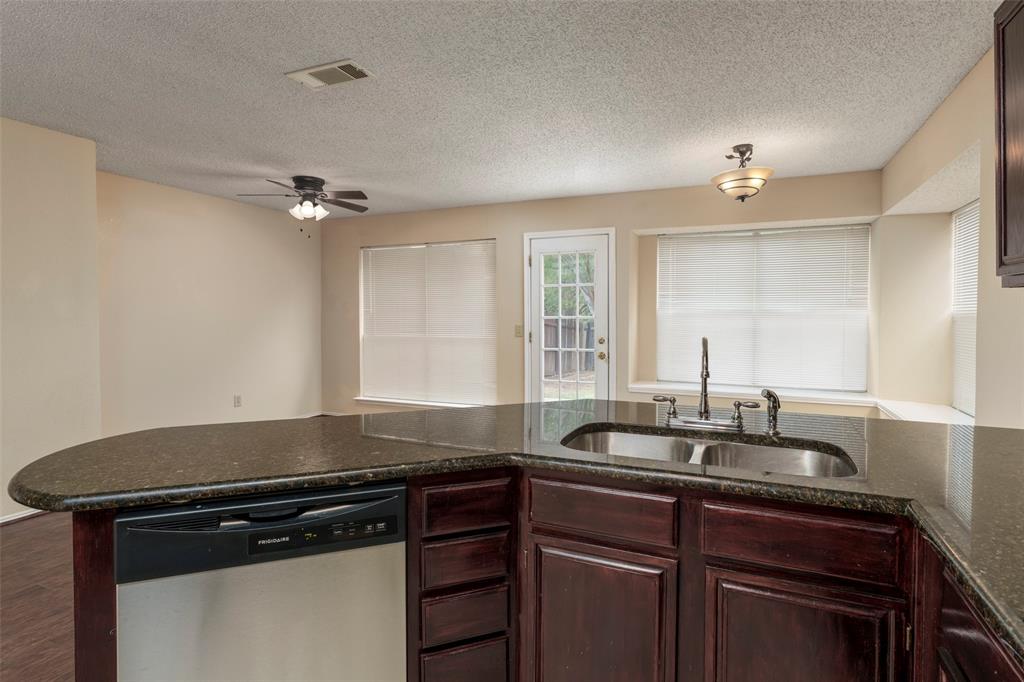 Kitchen island with a dark countertop, stainless steel dishwasher, and dark wood cabinetry