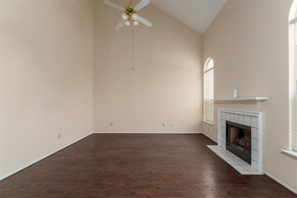 Vaulted ceiling, wood-finish flooring, fireplace with tile surround and hearth, arched window, and ceiling fan with light fixture