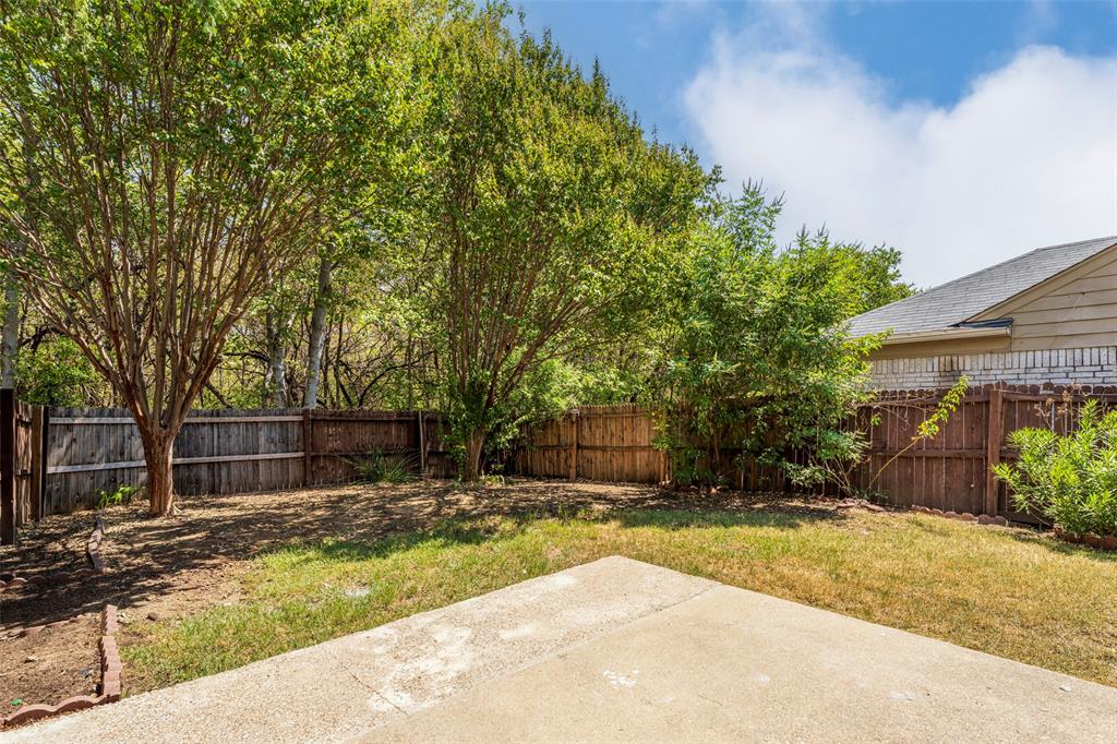 Rear exterior featuring a concrete patio, wood fencing, and mature trees