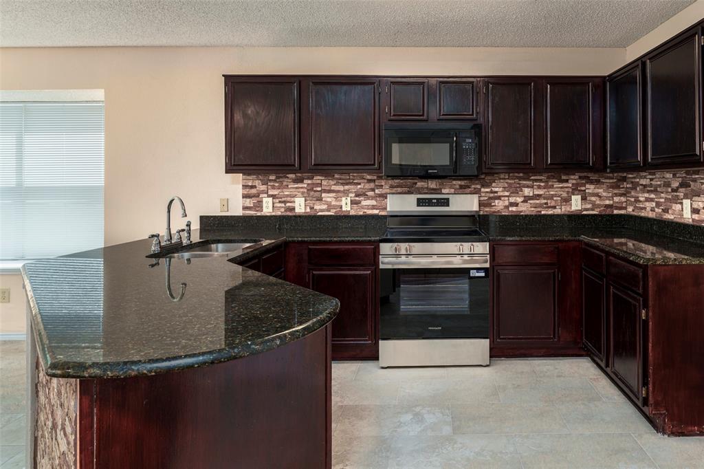 Kitchen with dark cabinetry, stone countertops, stainless steel appliances, a tile backsplash, and light-colored flooring