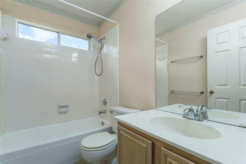 White tiled bathtub and shower combination with an overhead window, a vanity with an integrated sink, and an expansive wall mirror