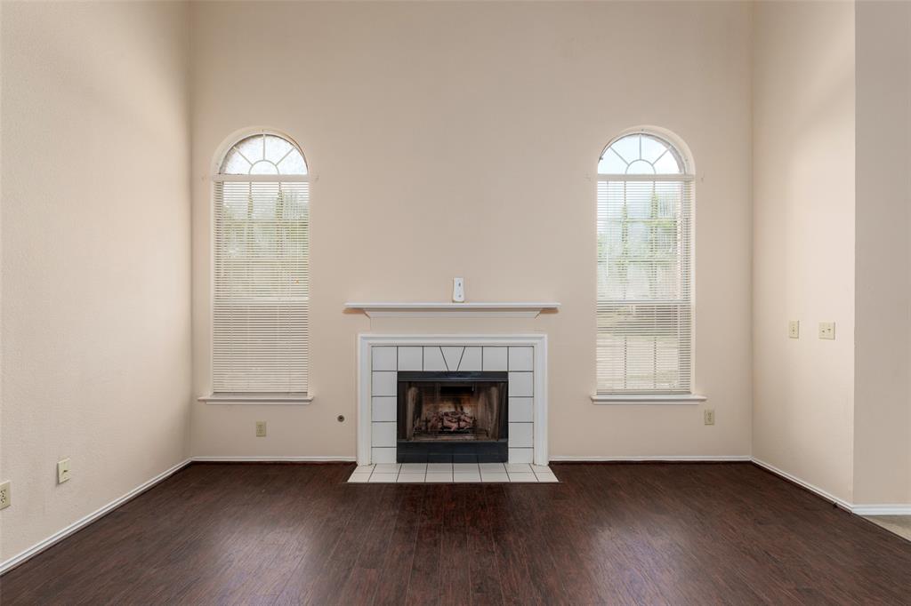 Vaulted ceiling with dual arched windows, fireplace with white tile surround, and rich wood-finish flooring