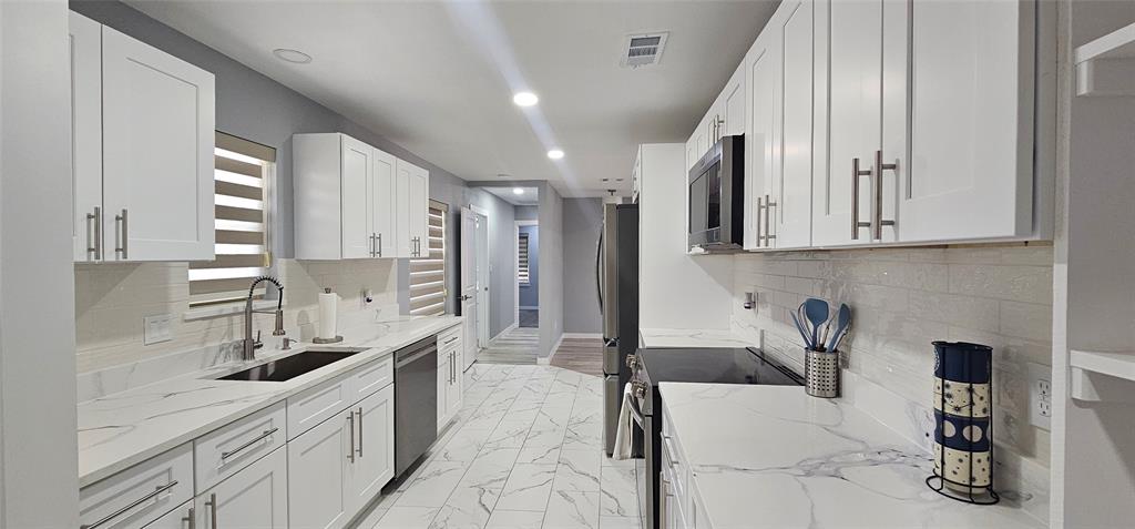 Galley kitchen featuring white shaker cabinetry, stainless steel appliances, a tile backsplash, light-toned countertops, and recessed lighting