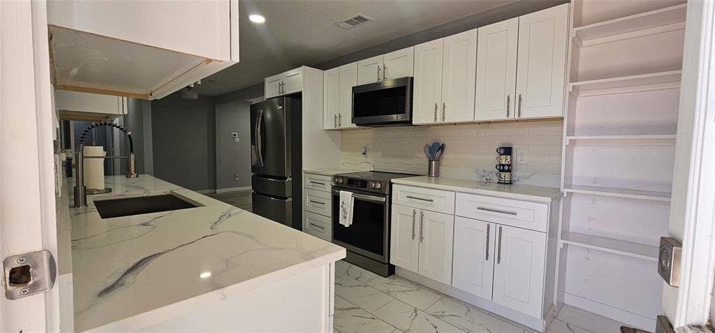 White cabinetry, stainless steel appliances, white patterned countertops, tile flooring, and integrated shelving