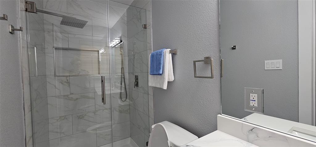 Glass-enclosed shower with tile surround, rain showerhead, and recessed shower niche
