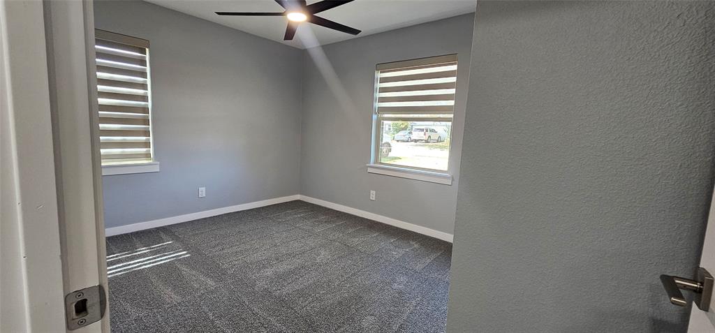Carpeted flooring, neutral wall tones, two windows with horizontal blinds, and a ceiling fan with integrated lighting