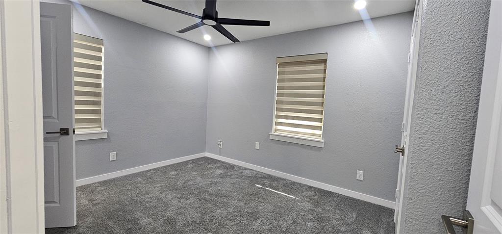 Modern ceiling fan with integrated lighting, recessed ceiling lighting, textured walls, two windows with horizontal blinds, and grey carpeting