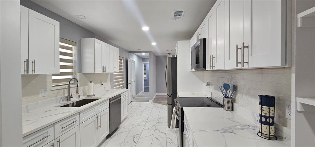 Galley kitchen featuring white cabinetry, integrated stainless steel appliances, a tile backsplash, and stone countertops