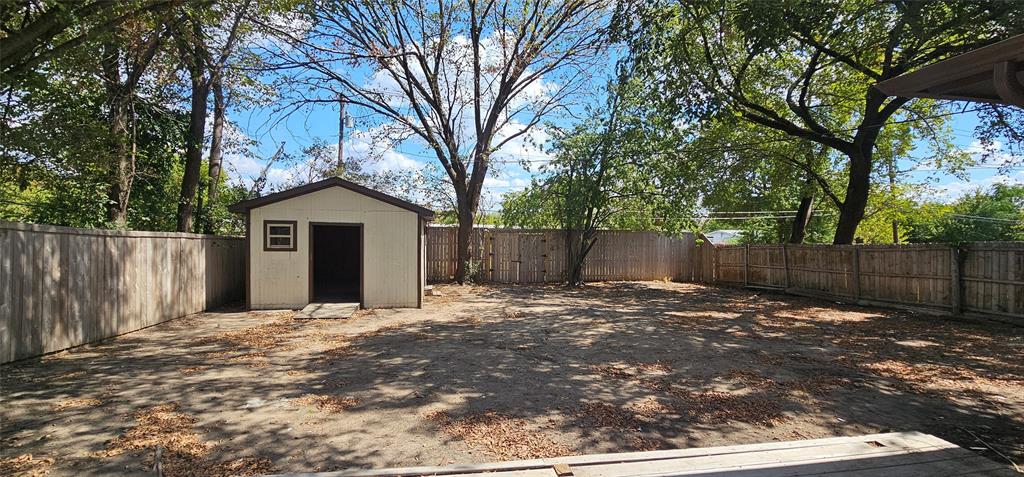 Expansive yard featuring a privacy fence, mature trees, and an exterior storage shed with a window