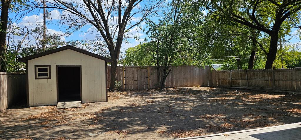 Expansive outdoor area featuring a storage shed, wood fencing, and mature trees