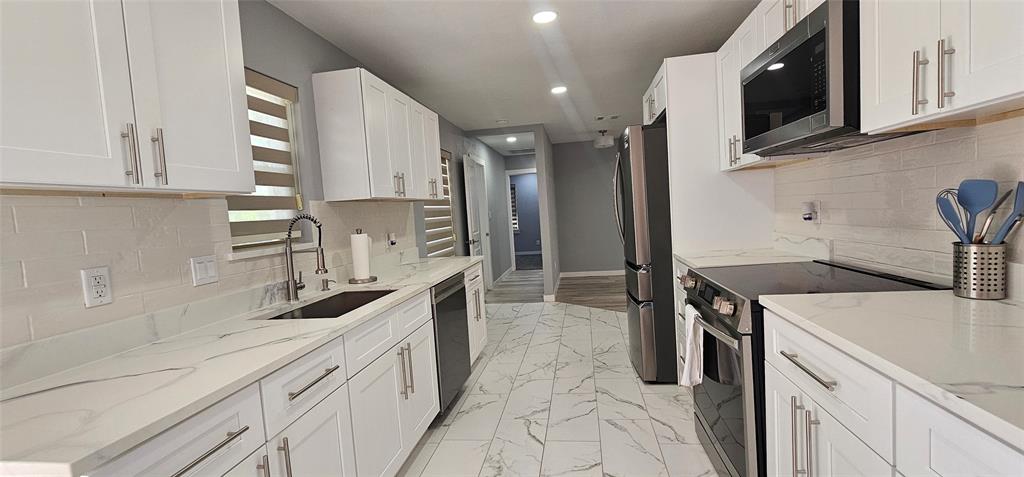 Kitchen featuring white cabinetry, light-toned countertops, stainless steel appliances, a tile backsplash, and patterned tile flooring