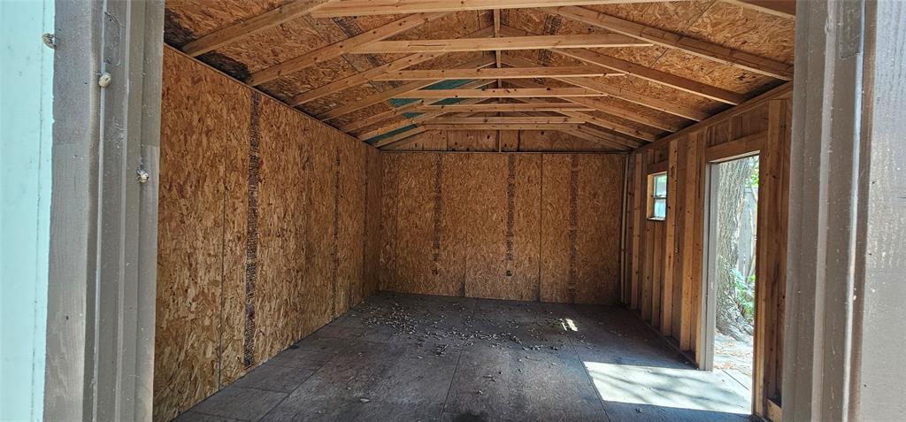 Vaulted ceiling with exposed wood framing, wood panel walls, and a single window for natural light