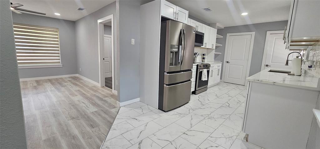 Modern kitchen with white cabinetry, stainless steel appliances, marble-look tile flooring, and light-toned countertops