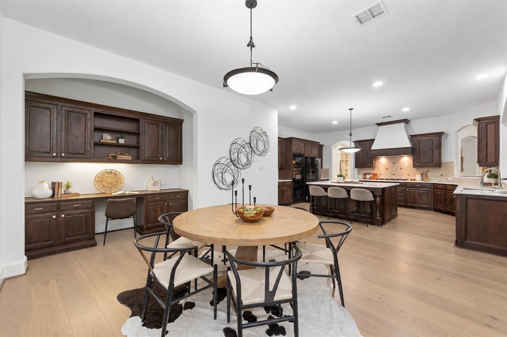 Open-concept layout featuring wood-finish flooring, a kitchen island with seating, dark wood cabinetry, a built-in desk area with shelving, and recessed lighting