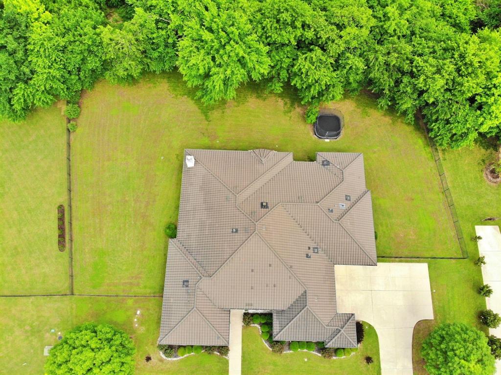 Expansive property featuring a tiled roof, extensive green space, mature perimeter trees, and a concrete driveway